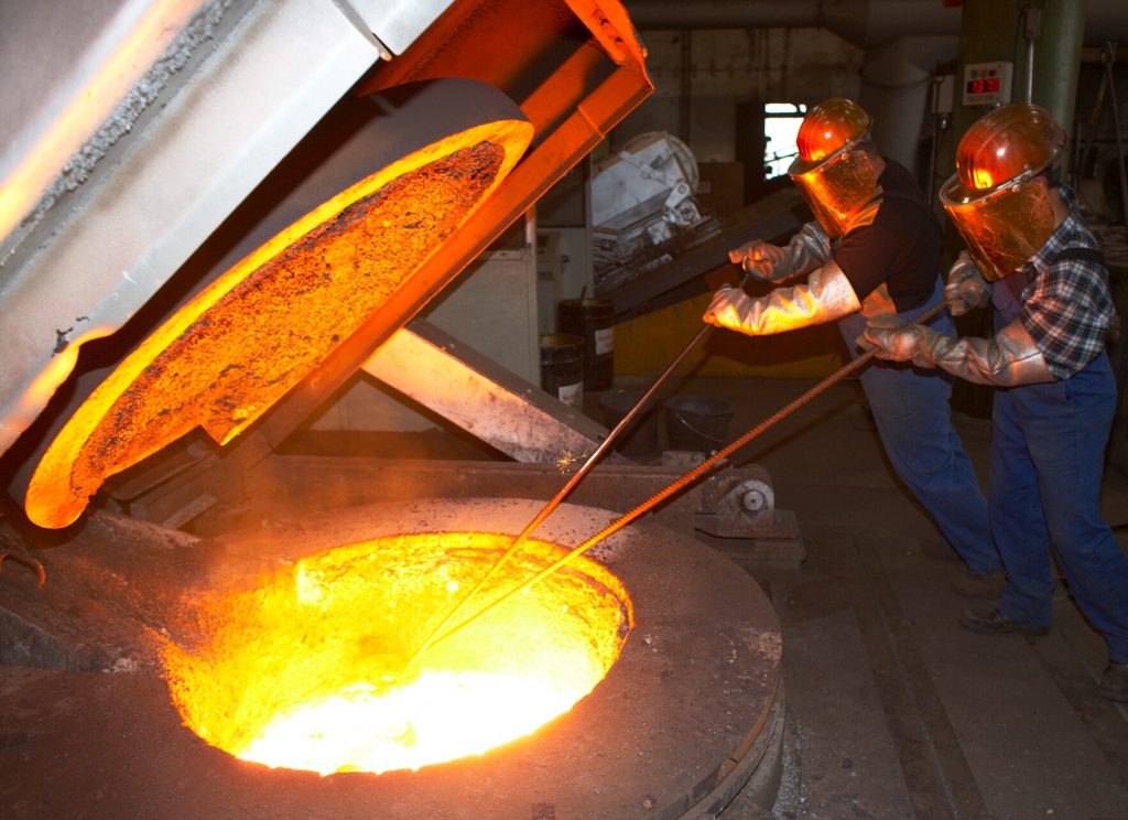 two steelworkers in a foundry with red hot furnace requiring industrial insulation